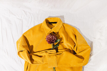 Yellow corduroy shirt and flower on a white textile background.