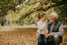 Grandfather Spending Time With His Granddaughter In Park On Autumn Day
