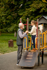 Wall Mural - Grandfather spending time with his granddaughter in park playground on autumn day