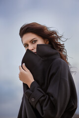 Outdoor portrait of Fashion model. Portrait of a young pretty woman in a coat on the autumn beach.  Beautiful brunette girl in cozy  dark coat sensually looking away on seaside.