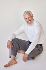 Smiling bearded mature older gray-haired business man, happy old senior stylish businessman wearing fashion clothes looking away laughing sitting barefoot on floor at white wall. Vertical