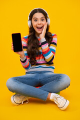 Canvas Print - Teenager girl use smart phone, share social media, chatting by mobile phone wear stylish casual trendy clothes isolated over yellow background. Kid showing blank screen mobile phone, mockup copyspace.