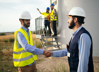 Two male engineers shake hands in a field of windmills. Agreement, renewable energy, energy transition