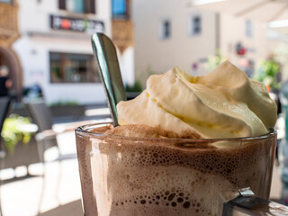 Close-up of a hot coffee drink with whipped cream on top. Enjoying time in a small caf´e outdoors. A full latte macchiato in a cup during vacation. Delicious brown beverage at lunchtime.