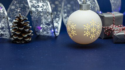 Wall Mural - illuminated christmas ball with small gift boxes and pine cone on blue background