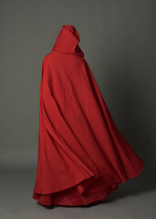 Wall Mural - Full length portrait of woman wearing red medieval fantasy costume, flowing hooded cloak. Standing pose in backview, gestural hand poses, walking away from camera isolated on grey studio background.