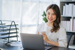 © Kritdanai - Beautiful Asian businesswoman working on a desk with a laptop with a smiling face while looking at the document received in the office.