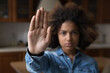 Serious African teenager girl looking at camera raises her palm showing stop gesture, against emotional and physical abuse, bullying at school, racial inequality, struggling for women rights, close up