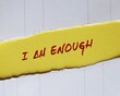 Ripped torn yellow paper with handwritten text I AM ENOUGH concept of self-acceptance, affirmation to tell yourself you are good enough and capable enough to become everything you want to be