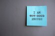 Blue note on gray wall with text I AM NOT GOOD ENOUGH with red crossing on NOT GOOD , concept of self worth , stop striving for approval, more valid , more loved or validation , you are good enough
