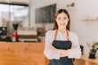 © Kritdanai - Opening a small business, AHappy Asian woman in an apron standing near a bar counter coffee shop, Small business owner, restaurant, barista, cafe, Online, SME, entrepreneur, and seller concept