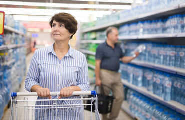 Mature woman considering bottle of vermouth in supermarket