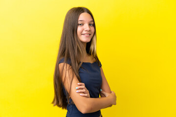 Poster - Little caucasian girl isolated on yellow background with arms crossed and looking forward