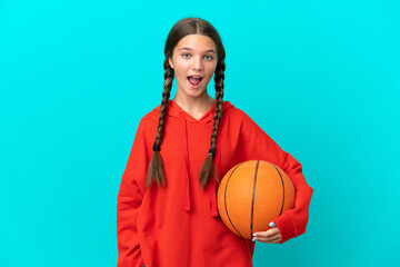 Wall Mural - Little caucasian girl playing basketball isolated on blue background with surprise facial expression