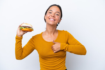 Wall Mural - Young hispanic woman holding a burger isolated on white background giving a thumbs up gesture