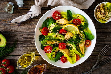 Wall Mural - Fresh vegetable salad - avocado, artichoke, lettuce, cherry tomatoes, cucumber, arugula and spinach on wooden table 