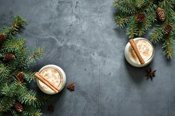 Eggnog in glasses with star anise, cinnamon, chrismas branch on gray concrete table. Copy space, flat lay composition. Christmas traditional drink. 