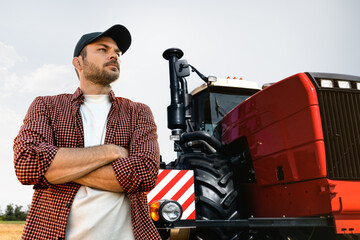 Poster - A bearded farmer in a cap and a plaid shirt stands in front of a agricultural tractor
