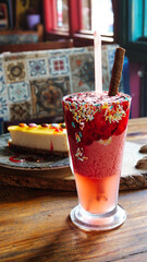 Wall Mural - A glass of strawberry smoothie and a slice of candy coated lemon cheesecake served at a cafe table.