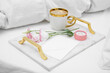 Tray with cup of coffee, flowers and beautiful engagement ring in box on white bed