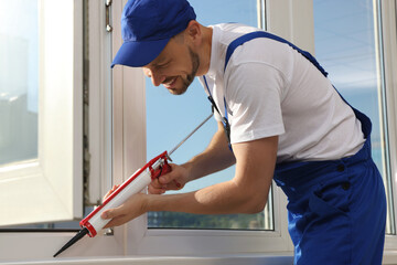 Wall Mural - Worker sealing plastic window with caulk indoors. Installation process