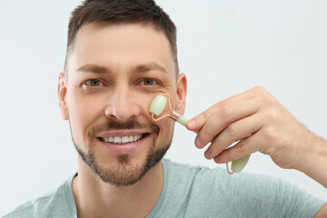 Man using nephrite facial roller on white background