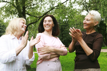 Women friends in the park celebrate a birthday. Clap your hands, congratulate, rejoice. Happy summer day. The concept of friendship, happy old age and emotions.