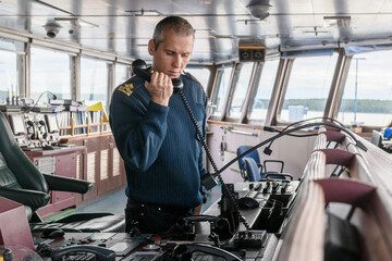 Wall Mural -  Deck officer on watch during cargo operations. Man in white overall with VHF radio. Commercial shipping. Cargo ship.