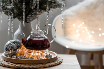 Wall Mural - A bouquet of fir branches with icicles, candles and a teapot with tea on a wooden table in the home interior of the living room. Cozy concept of festive drinks.