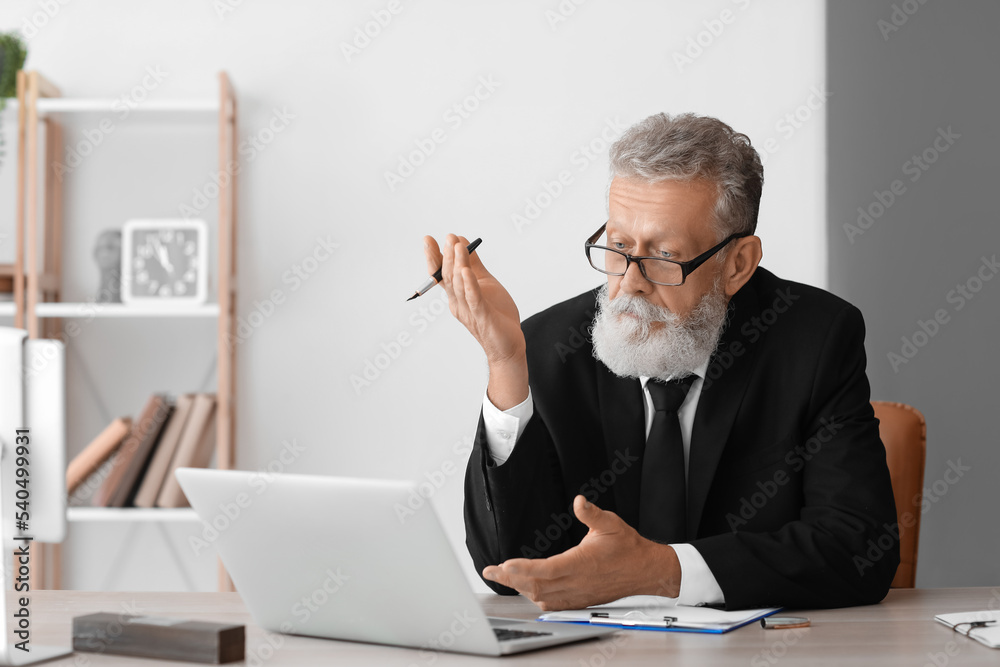 Male psychologist with laptop video chatting at table in office