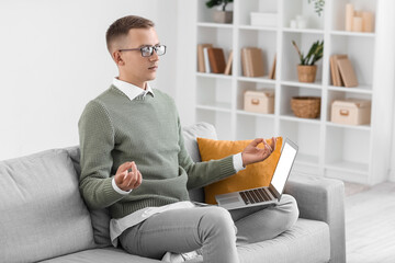 Poster - Young man with laptop meditating on sofa at home