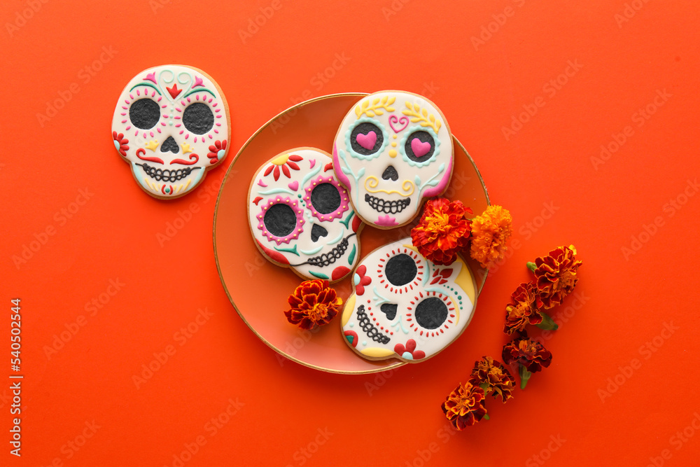 Plate with skull shaped cookies and flowers on red background. El Dia de Muertos