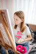 © Анна Молько - a girl in a white T-shirt paints with paints on a canvas on an easel. drawing at home.