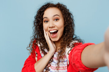 Sticker - Close up young fun woman of African American ethnicity wear red jacket do selfie shot pov on mobile cell phone hold face isolated on plain pastel blue cyan background. Wet fall weather season concept.