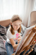 © Анна Молько - a girl in a white T-shirt paints with paints on a canvas on an easel. drawing at home.