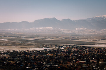 Panoramic view over the ski slope Poiana Brasov ski resort in Transylvania, Pine forest covered in snow on winter season,Mountain landscape in winter with the Bucegi Mountains in the background.