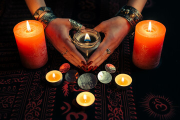 Women's hands  with bracelets and rings holding a burning candle in the dark. 