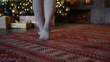 Low Angle Rear View Of Female Legs In Grey Knee Highs Walking To Christmas Tree And Standing Tiptoe. Selective Focus. Real Time Video. Tracking Shot. Winter Holidays Mood Theme.