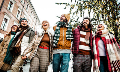 Smiling friends walking embraced on the city - Happy group of young people enjoying the day standing outside in winter clothes - Friendship concept with boys and girls laughing during xmas holidays