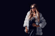 Fashion blonde girl posing in luxurious fur coat and sunglasses while standing on black background
