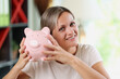 Smiling woman holding pink piggy bank in hands