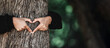 Young woman hug a tree in the forest and show a sign of heart and love for nature with copy space