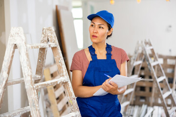 Asian woman builder checking project documentation while working in apartment.