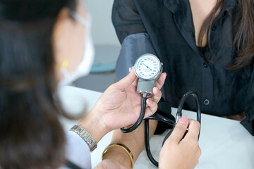 Doctor checking blood pressure of female patient with manual blood pressure monitor, medical concept