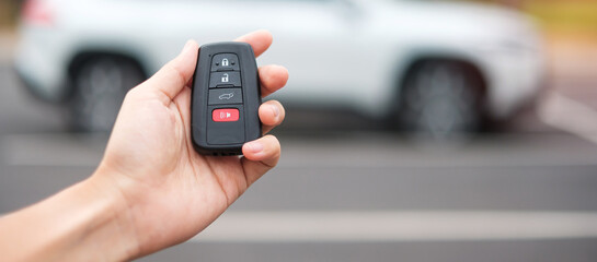 Hand holding car remote control, smart key to lock or unlock doors of white car. Safety, travel and transportation concept