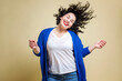 A young woman dances joyfully. Beautiful curly brunette with flowing hair in jeans, a blue sweater and a white tank top. Positivity and happiness. Yellow background.