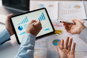 Business team together to make investment planning on digital tablet at the meeting. Close-up of a business consultant pointing to graphs and charts analyzing company growth to expand the product line