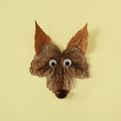 Wall Mural - Wolfs head made of autunmn leaves and chestnut on yellow background