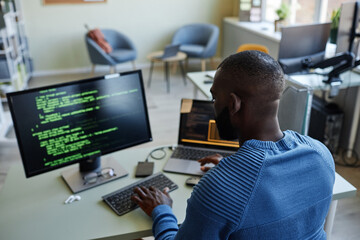 Wall Mural - Back view of African American software developer writing code at workplace in office with multiple devices