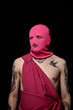 © Clique Images - Portrait of young man in pink mask with tattoos on his body standing against black background